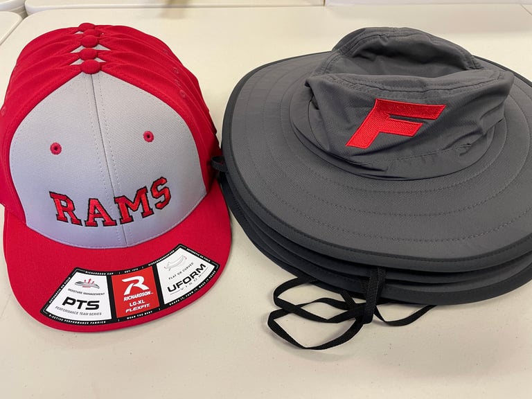 Red and white Rams baseball cap and gray wide-brim sun hat with red logo displayed side by side on white surface