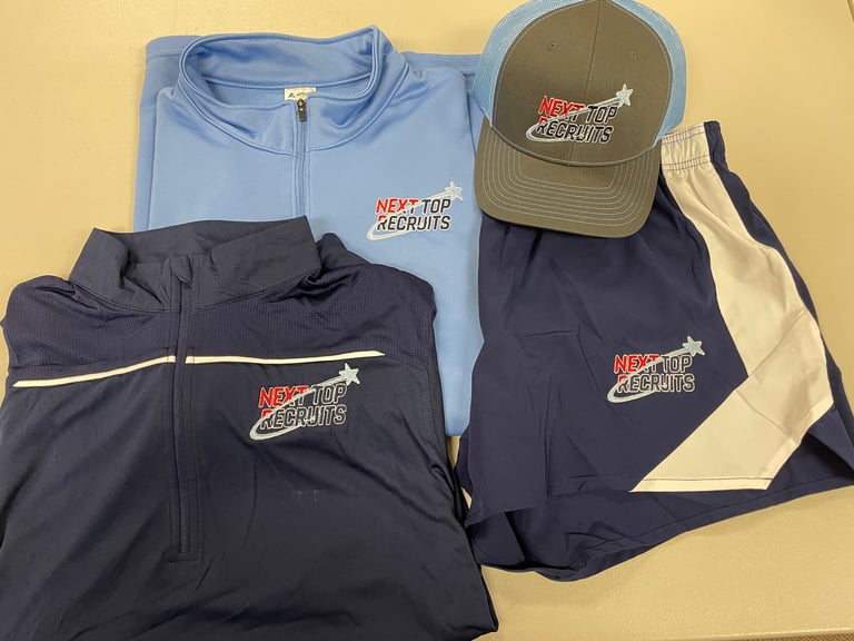 Collection of Next Top Recruits branded sportswear including blue and black jackets, cream and navy athletic pants, and olive baseball cap on yellow background