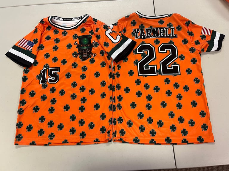 Two orange baseball jerseys with black shamrock pattern and player numbers displayed side by side